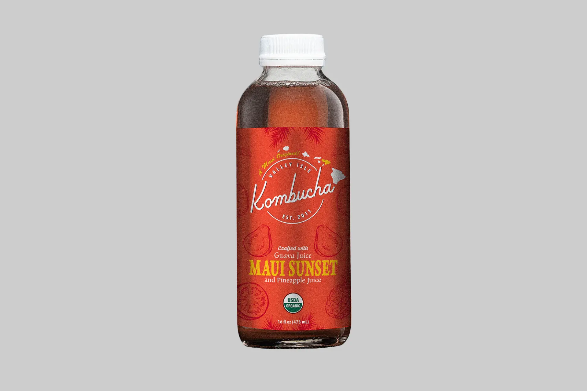 A bottle of Valley Isle Kombucha Maui Sunset against a backdrop of tropical fruits like pineapple and guava, with a Hawaiian beach scene. - Product Review